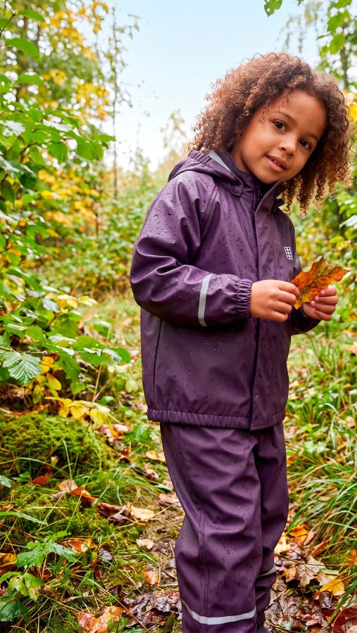 Child in purple rainwear exploring an autumn woodland
